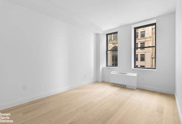 spare room featuring radiator, light wood finished floors, and baseboards
