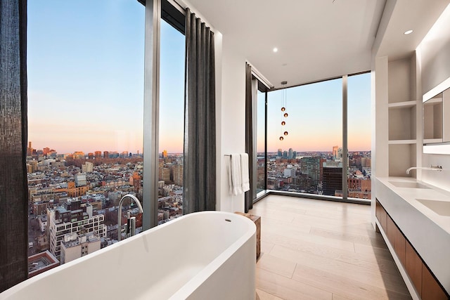 bathroom with expansive windows, a view of city, a freestanding tub, wood finished floors, and recessed lighting
