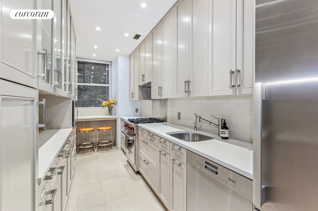 kitchen with high end appliances, a sink, backsplash, light countertops, and recessed lighting