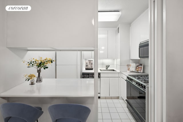 300 E 40th St Unit 10N, New York City, NY 10016 - kitchen with range with gas stovetop, a sink, white cabinets, light countertops, and light tile patterned floors