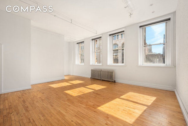 empty room with radiator, rail lighting, hardwood / wood-style flooring, and baseboards