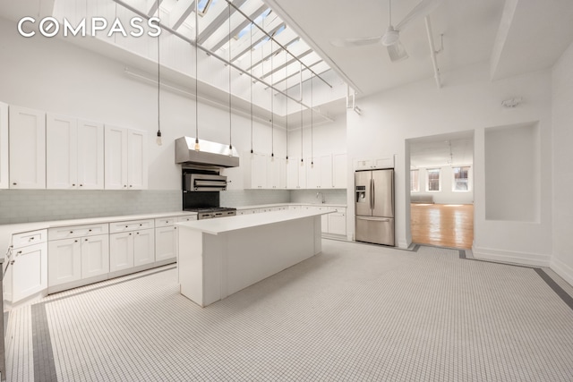 kitchen featuring stainless steel refrigerator with ice dispenser, a towering ceiling, under cabinet range hood, light countertops, and white cabinetry