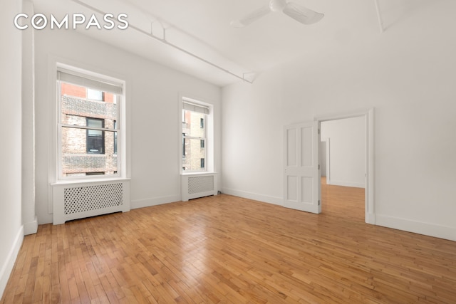 empty room with light wood finished floors, radiator, a ceiling fan, and baseboards