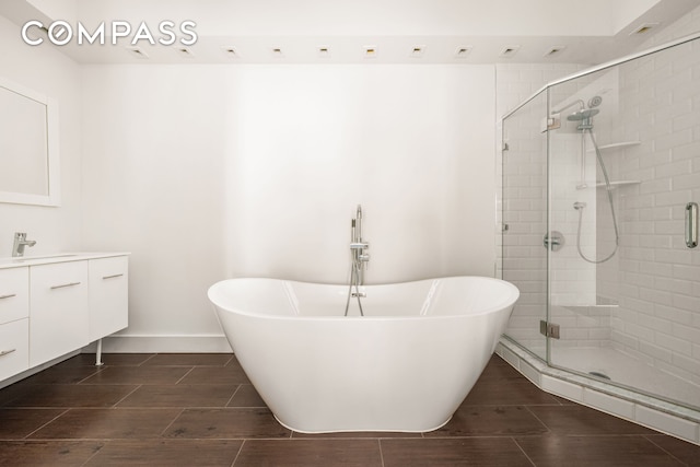 full bathroom featuring vanity, a shower stall, a freestanding bath, and baseboards