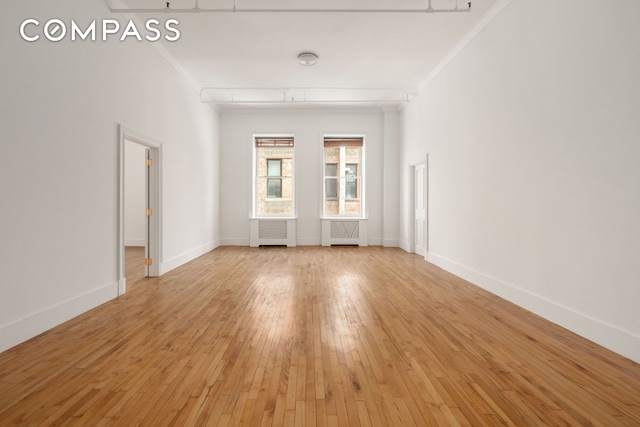 spare room with light wood-type flooring, radiator heating unit, baseboards, and ornamental molding