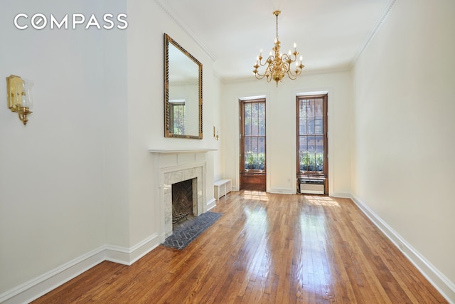 unfurnished living room with a chandelier, wood-type flooring, a fireplace, ornamental molding, and baseboards