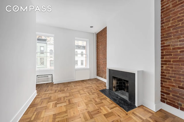 unfurnished living room with brick wall, baseboards, an AC wall unit, and a fireplace with flush hearth