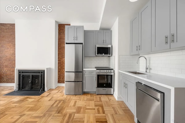 151 W 80th St Unit 4F, New York City, NY 10024 - kitchen featuring stainless steel appliances, gray cabinetry, a sink, light countertops, and brick wall