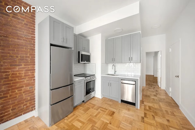 kitchen featuring stainless steel appliances, gray cabinets, a sink, light countertops, and baseboards