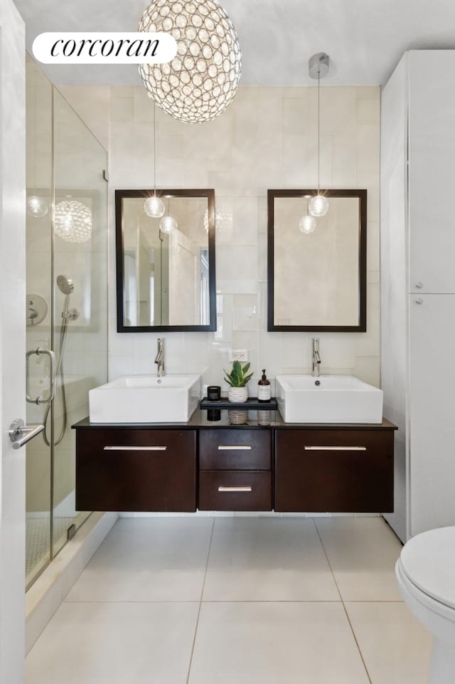 bathroom featuring a stall shower, double vanity, tile patterned floors, tile walls, and toilet