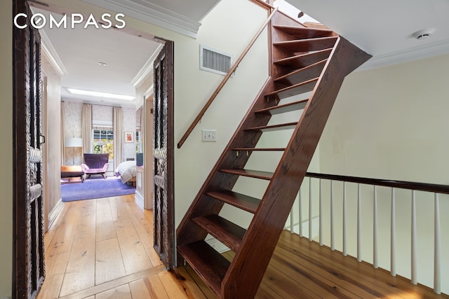 stairs with hardwood / wood-style flooring, wallpapered walls, and ornamental molding