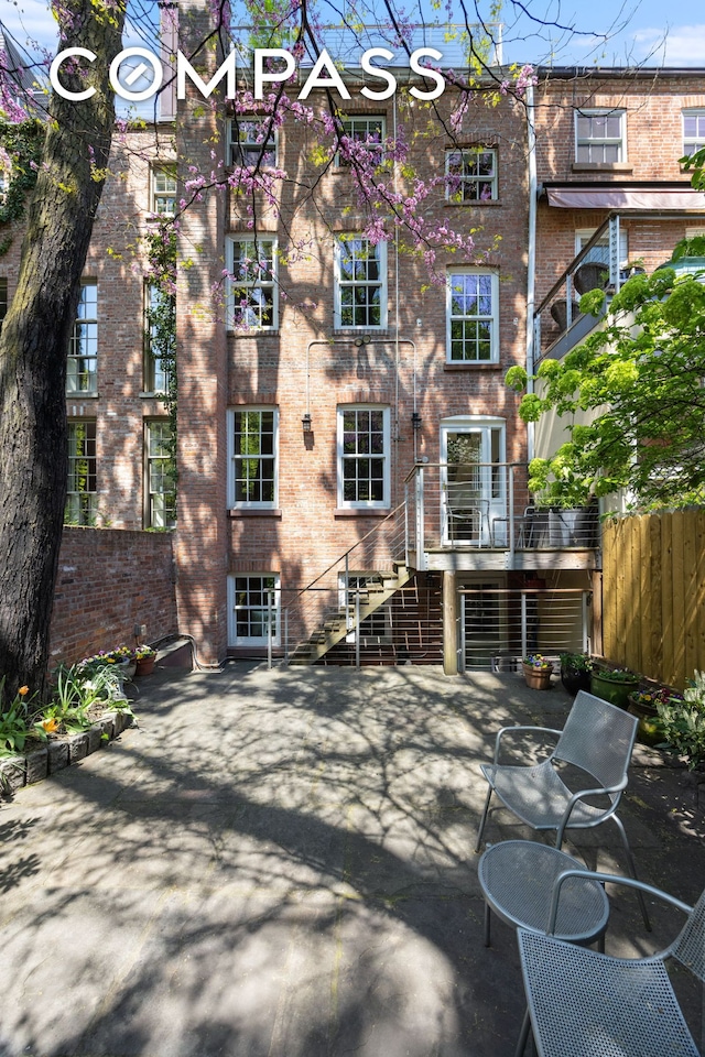 back of property featuring brick siding, a patio area, fence, and stairs