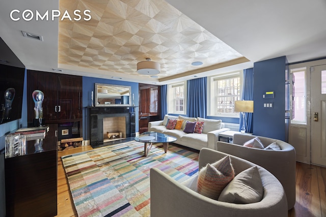 living room with a raised ceiling, wood finished floors, and a fireplace with flush hearth
