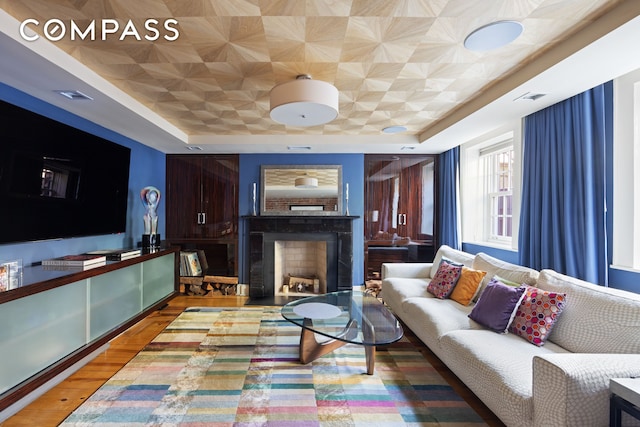living room with a raised ceiling, wood finished floors, and a fireplace with flush hearth