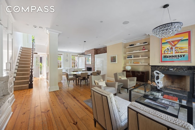 living area featuring a fireplace, a chandelier, crown molding, stairs, and light wood finished floors