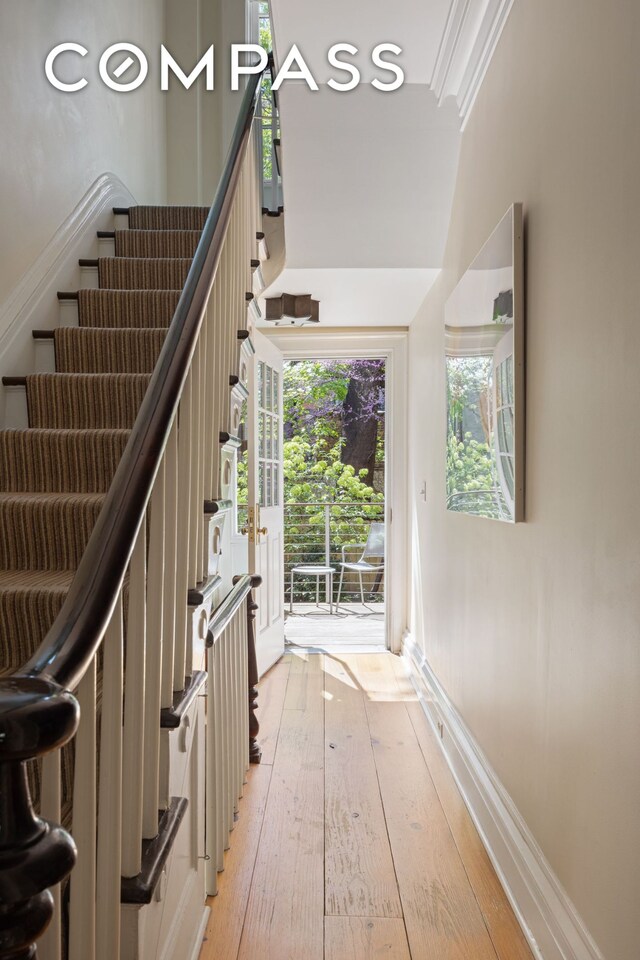stairs with baseboards, wood-type flooring, and crown molding