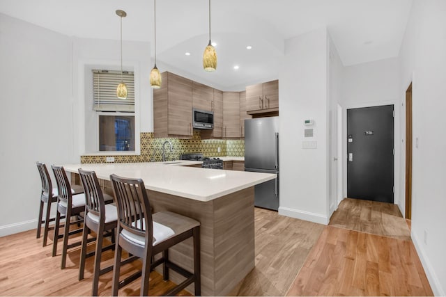 kitchen with appliances with stainless steel finishes, a peninsula, a breakfast bar area, light wood-style flooring, and tasteful backsplash
