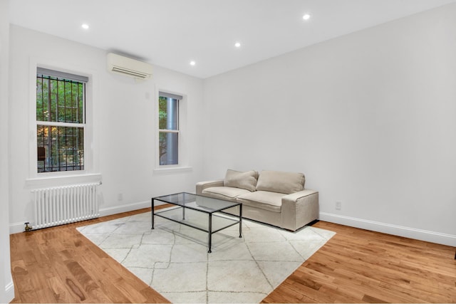 living room with radiator, an AC wall unit, wood finished floors, baseboards, and recessed lighting