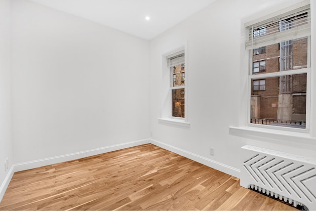 spare room with radiator heating unit, baseboards, light wood-type flooring, and recessed lighting
