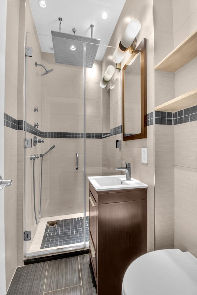 bathroom featuring vanity, a stall shower, toilet, tile walls, and recessed lighting