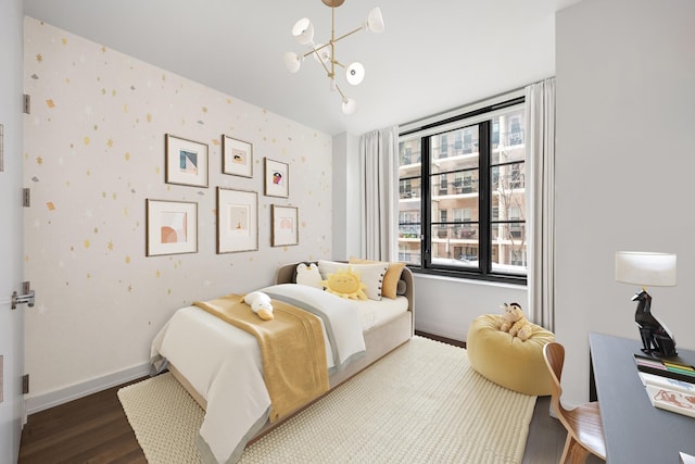 bedroom featuring wood finished floors, a chandelier, baseboards, and wallpapered walls