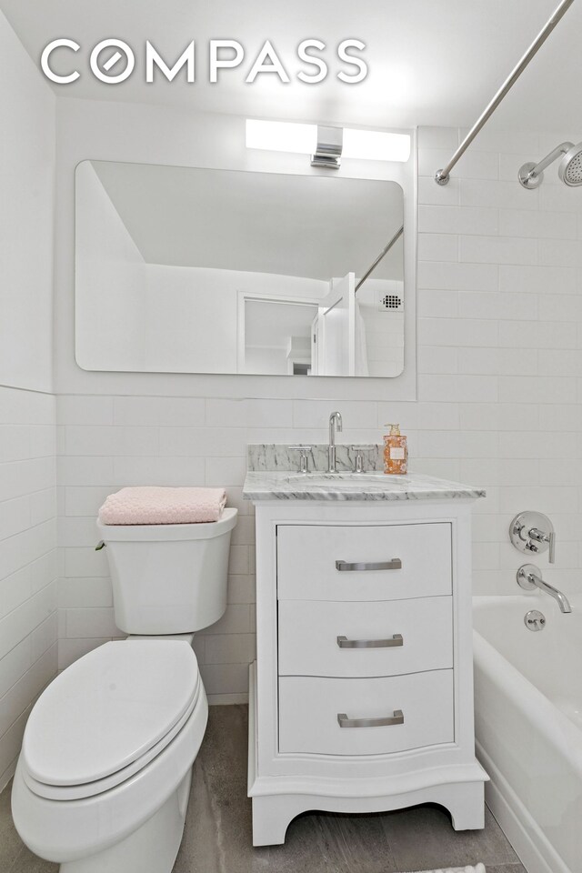 full bathroom featuring bathtub / shower combination, vanity, toilet, and tile walls
