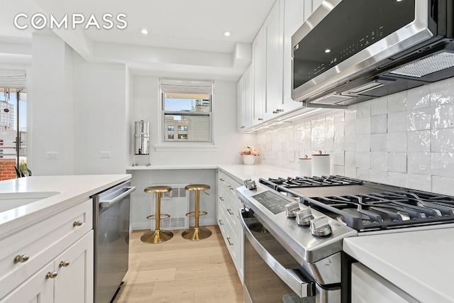 kitchen featuring stainless steel appliances, light wood-style flooring, backsplash, white cabinetry, and light countertops