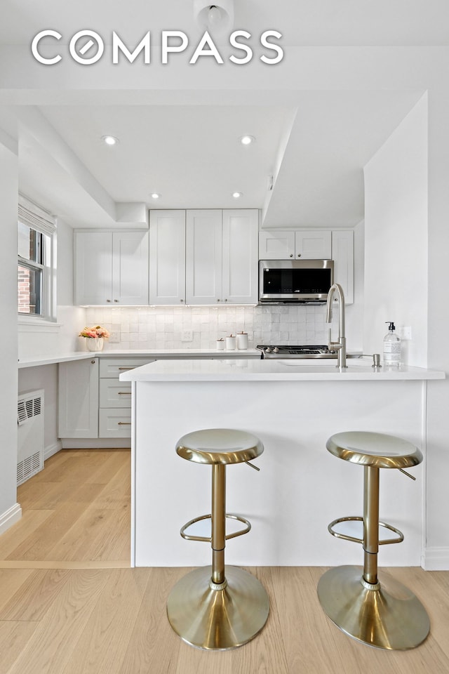 kitchen with stainless steel microwave, a kitchen bar, radiator heating unit, tasteful backsplash, and recessed lighting