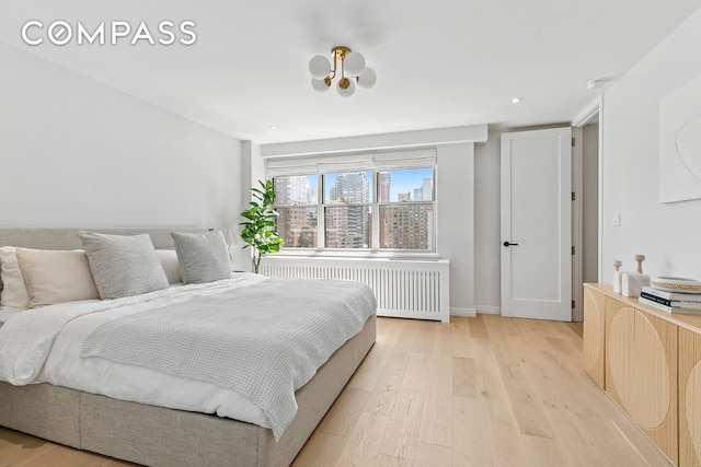 bedroom featuring radiator, light wood-type flooring, baseboards, a city view, and recessed lighting