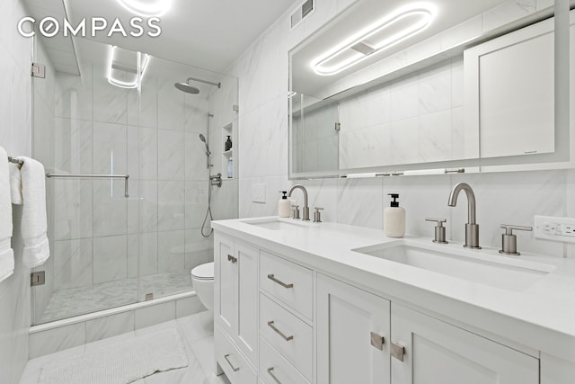 bathroom featuring toilet, a shower stall, double vanity, and tile walls