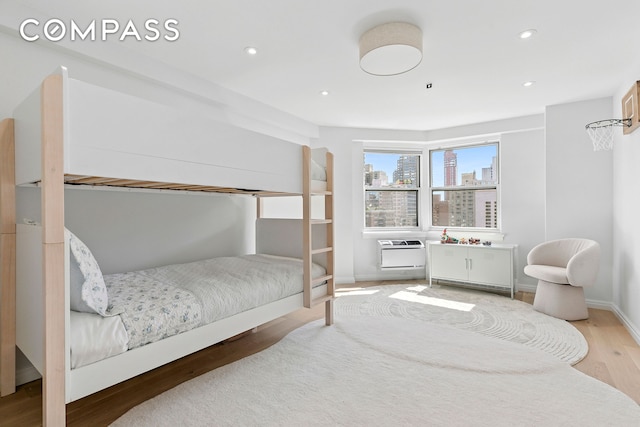bedroom featuring light wood-style floors, recessed lighting, a wall mounted AC, baseboards, and a city view