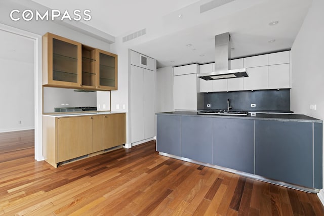 101 Warren St Unit 11L, New York City, NY 10007 - kitchen featuring island range hood, wood finished floors, modern cabinets, a peninsula, and glass insert cabinets