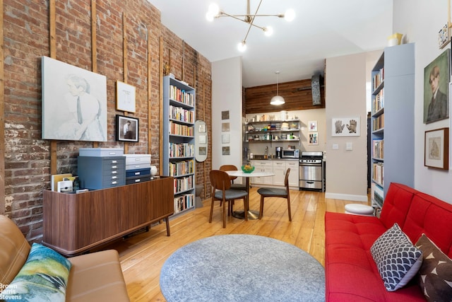 living area featuring light wood-style flooring, a chandelier, brick wall, and baseboards
