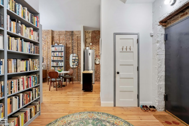 living area with brick wall, wood-type flooring, wall of books, and baseboards