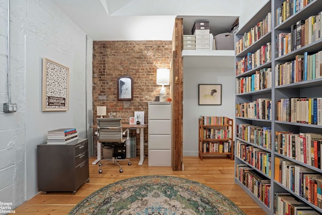 office with wall of books, hardwood / wood-style flooring, and brick wall