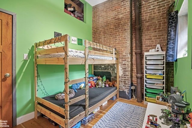bedroom featuring wood finished floors, brick wall, and baseboards