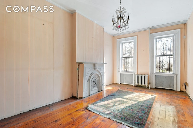 living room with ornamental molding, a chandelier, hardwood / wood-style floors, radiator, and a fireplace with flush hearth