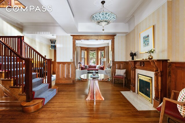 foyer with wood finished floors, wallpapered walls, a wainscoted wall, stairway, and a high end fireplace