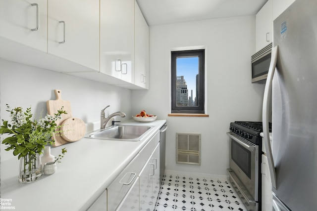 kitchen featuring appliances with stainless steel finishes, a sink, white cabinets, light countertops, and baseboards
