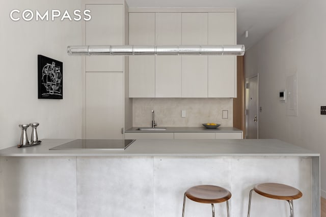 kitchen with black electric cooktop, a sink, tasteful backsplash, and white cabinetry