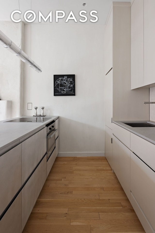 kitchen featuring a sink, light wood finished floors, white cabinetry, and light countertops