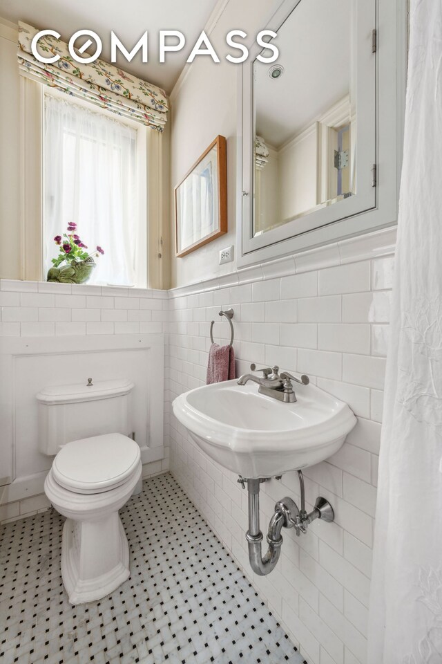 bathroom featuring tile walls, toilet, wainscoting, and tile patterned floors