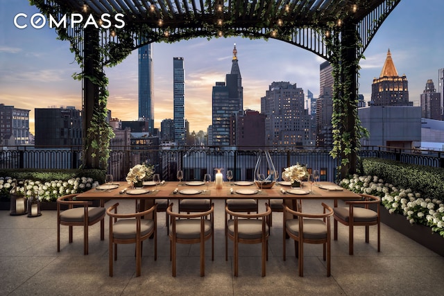 patio terrace at dusk featuring a skyline view, fence, and outdoor dining area