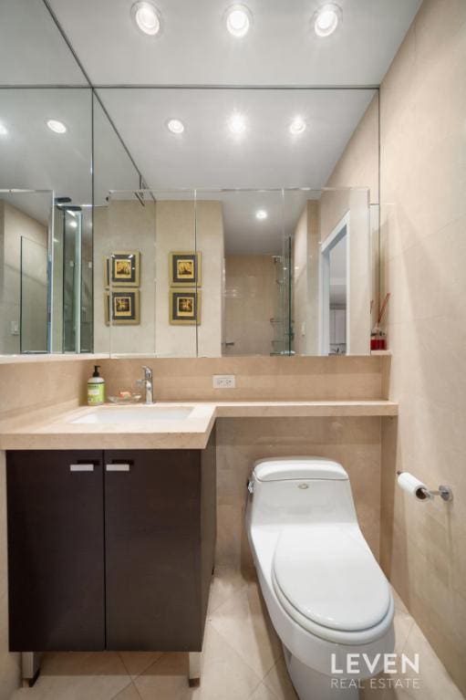 bathroom with tile patterned flooring, toilet, vanity, recessed lighting, and tile walls