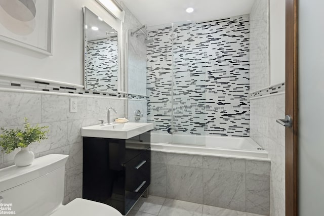 bathroom featuring toilet, tile walls, vanity, tiled shower / bath combo, and recessed lighting
