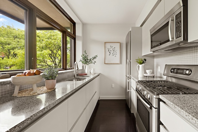 kitchen featuring stainless steel appliances, a sink, baseboards, tasteful backsplash, and white cabinetry