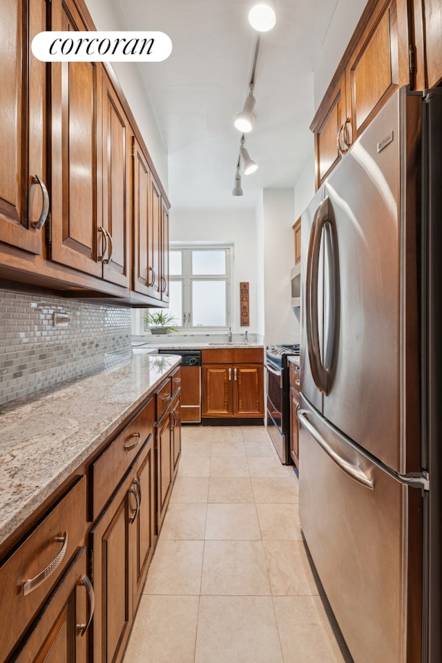 kitchen featuring stainless steel appliances, brown cabinets, decorative backsplash, light tile patterned floors, and track lighting