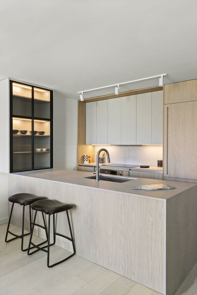kitchen featuring a sink, modern cabinets, a kitchen breakfast bar, light countertops, and light wood-style flooring