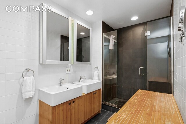 bathroom with tile walls, a stall shower, tile patterned floors, double vanity, and tasteful backsplash