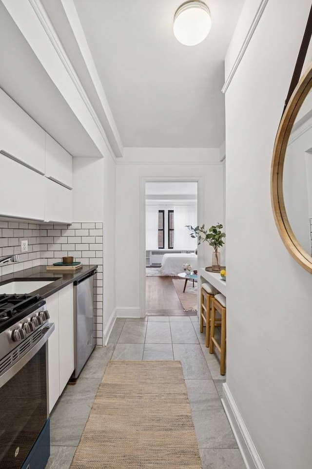 kitchen with stainless steel appliances, dark countertops, white cabinetry, backsplash, and baseboards